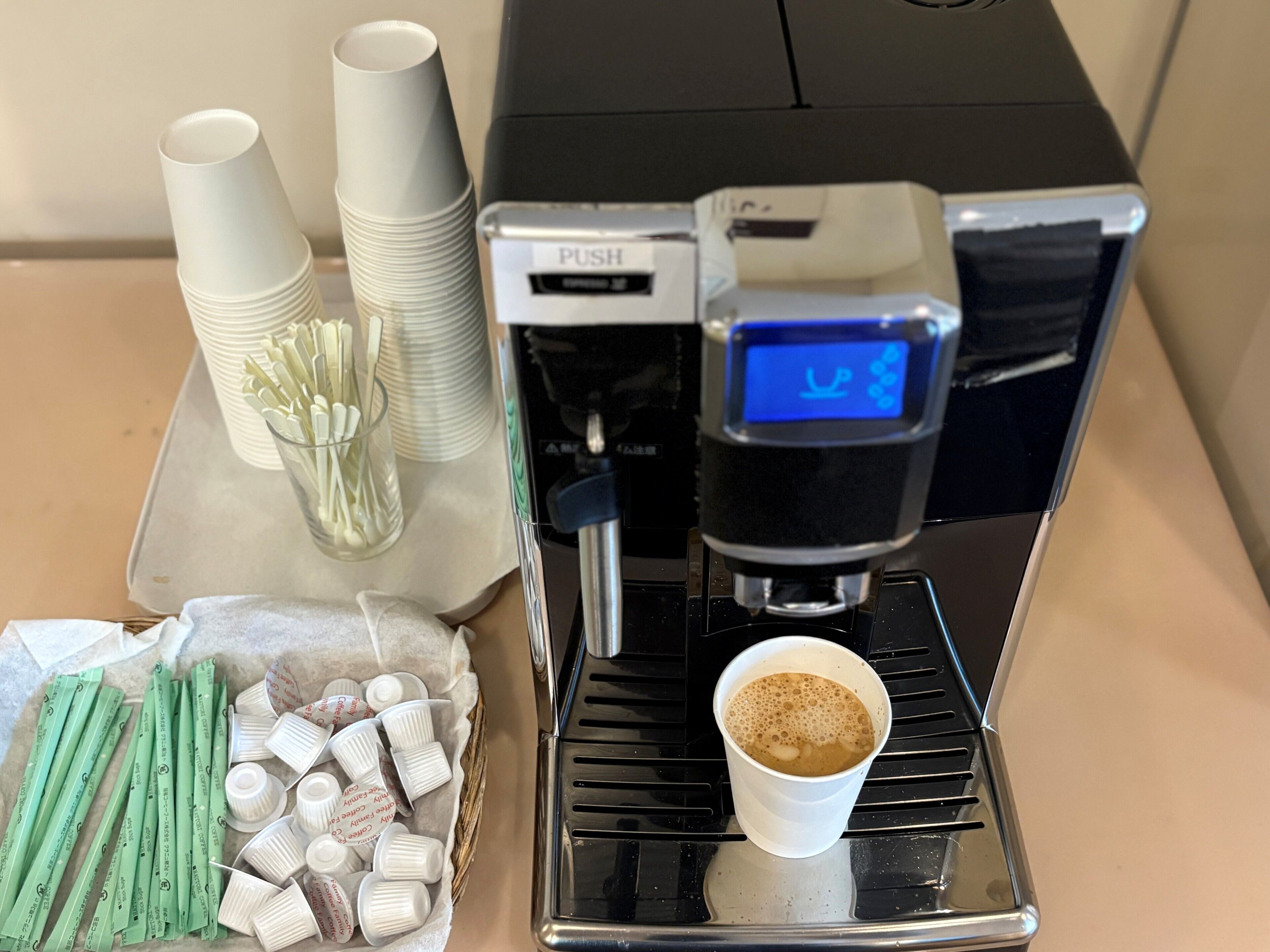 A coffee machine with a digital display, disposable cups, and coffee pods.