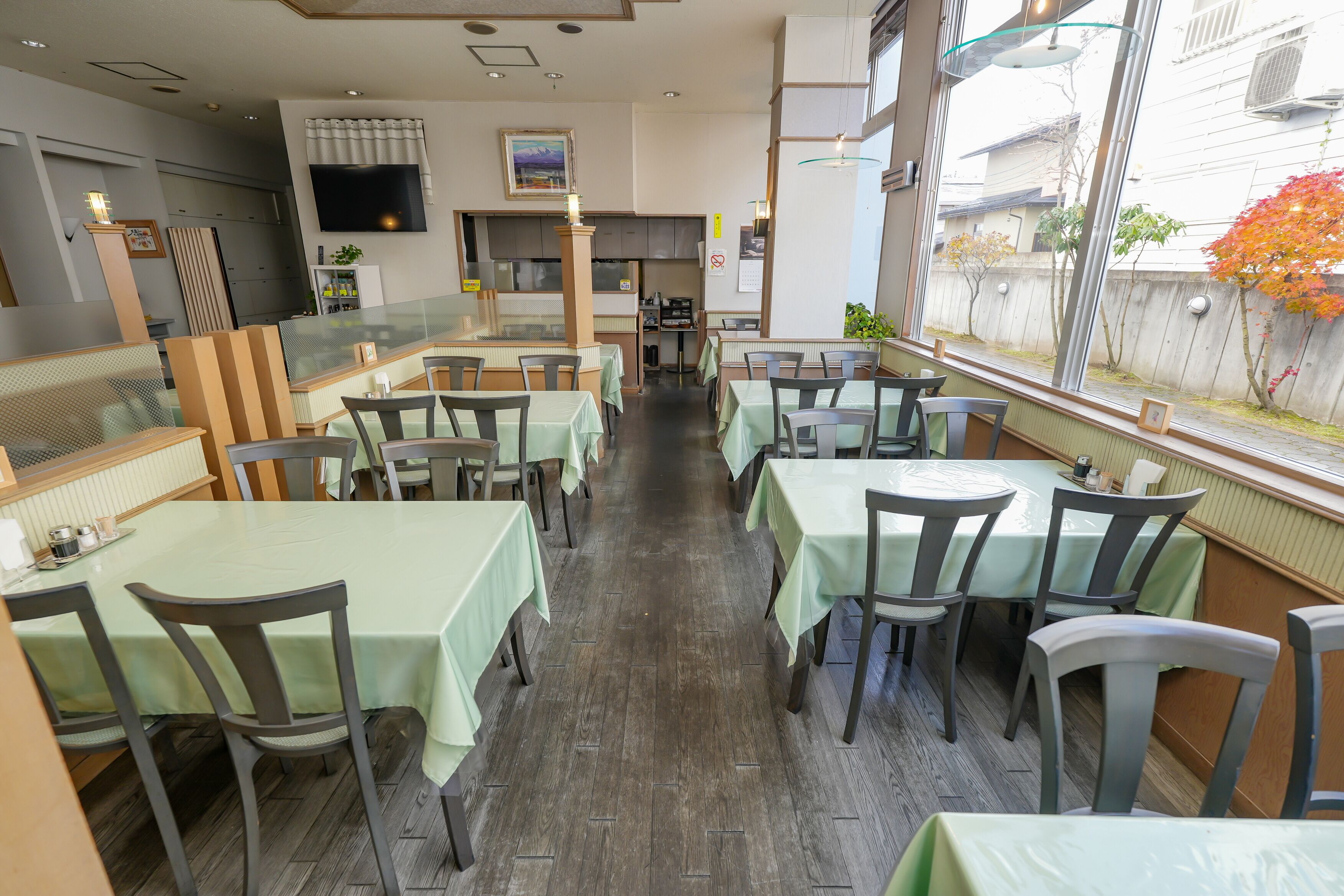 Un ristorante con tavoli e sedie, una zona cucina e un'ampia finestra che si affaccia all'esterno.