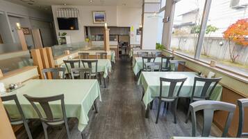 Un ristorante con tavoli e sedie, una zona cucina e un'ampia finestra che si affaccia all'esterno.