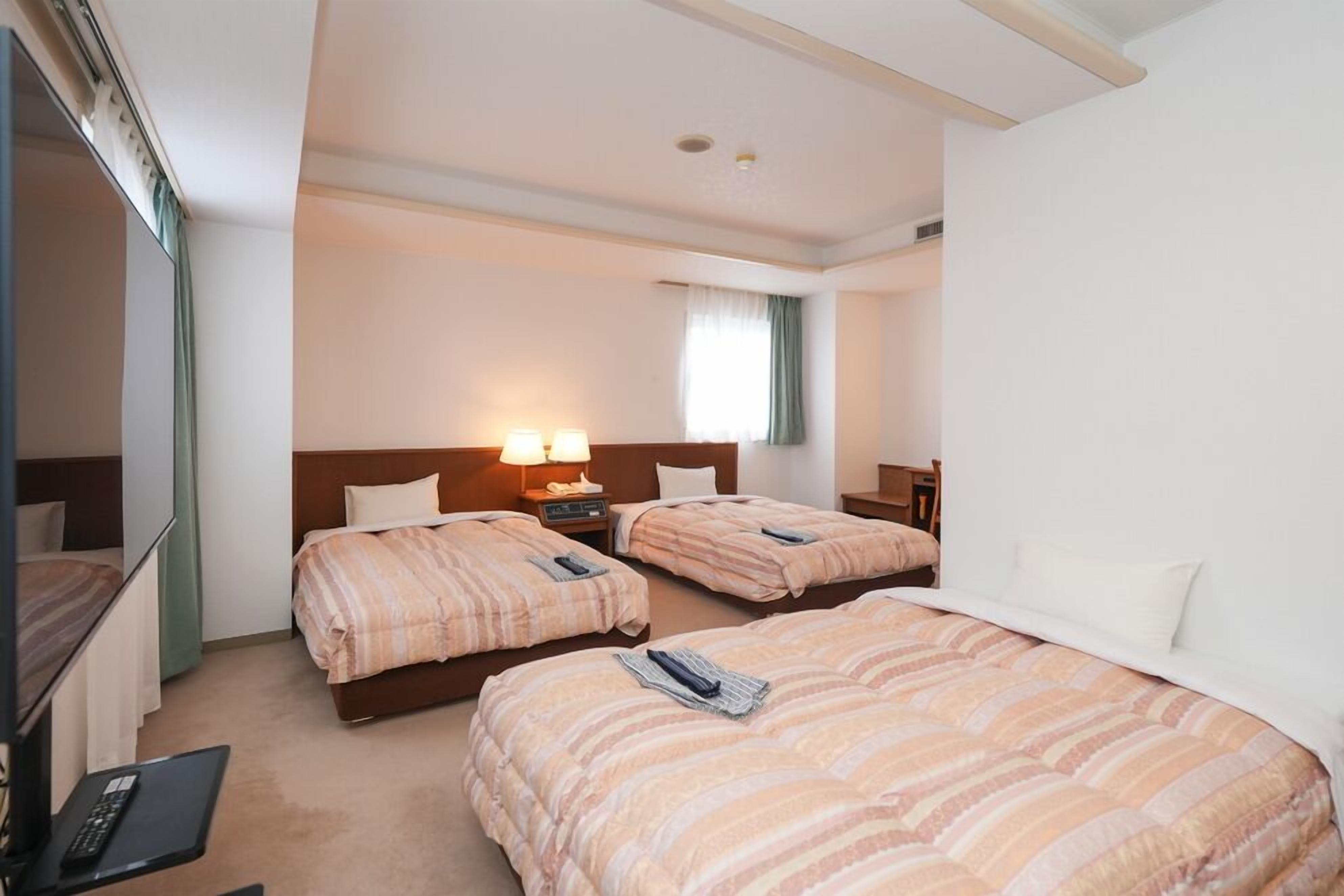 A hotel room with two beds, a TV, and a desk.
