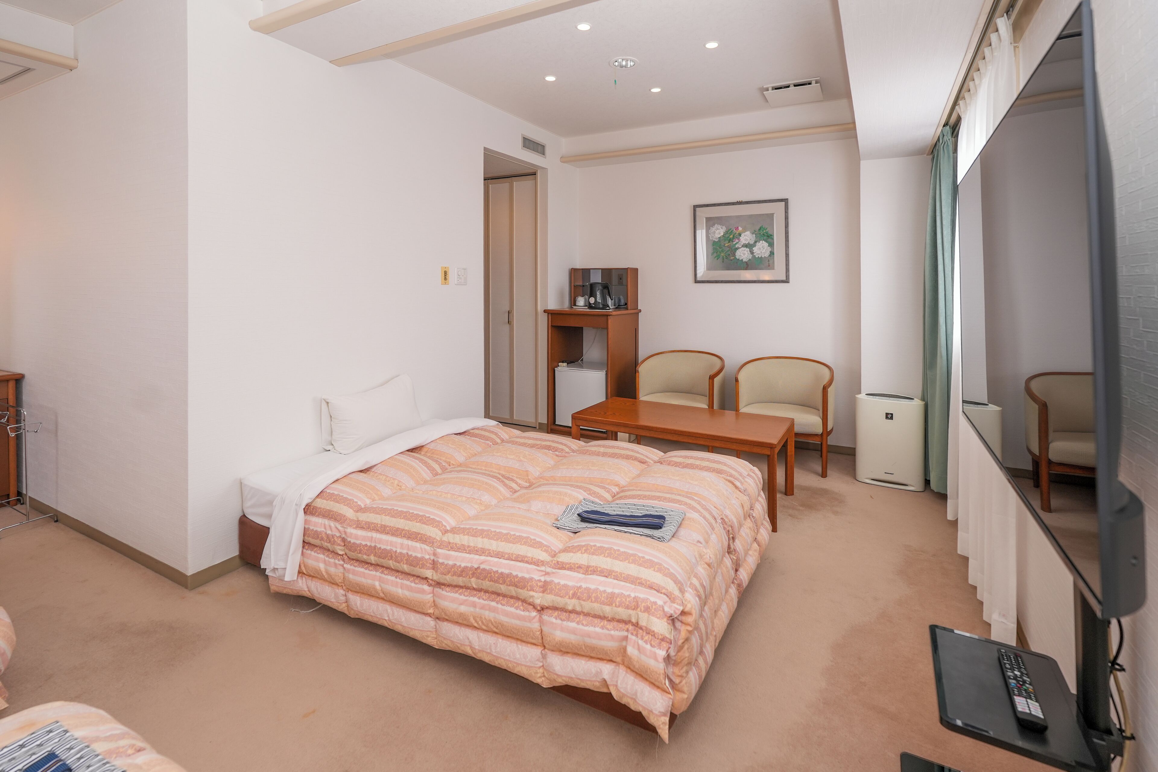 Een hotelkamer met een groot bed, een bureau, twee stoelen, een bijzettafeltje, een televisie en een radiator.