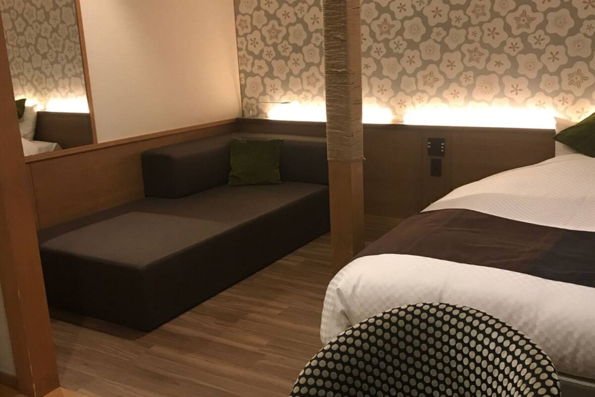 A bedroom with a bed, a sofa bed, a nightstand, and a wall-mounted lamp.