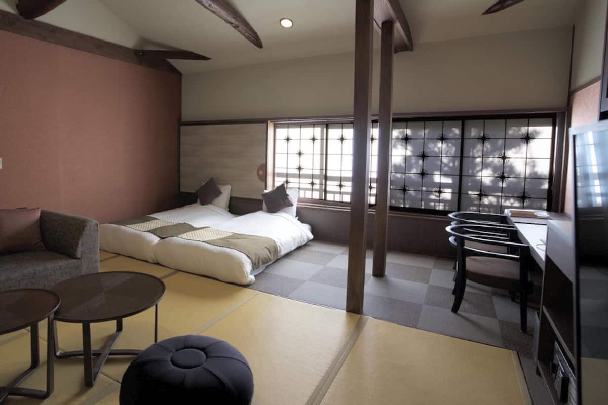 A modern hotel room with a bed, sofa, small tables, and a tatami mat floor.