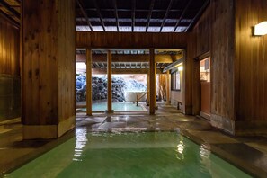 Un intérieur en bois avec un espace piscine central, des murs en pierre et une vue sur un jardin de rocaille extérieur.