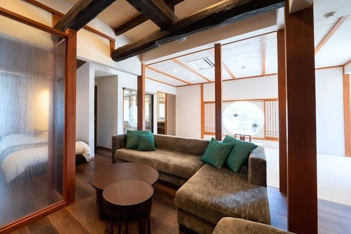 A traditional Japanese-style room with tatami flooring, a low wooden table, a sofa with cushions, and a sliding glass door.