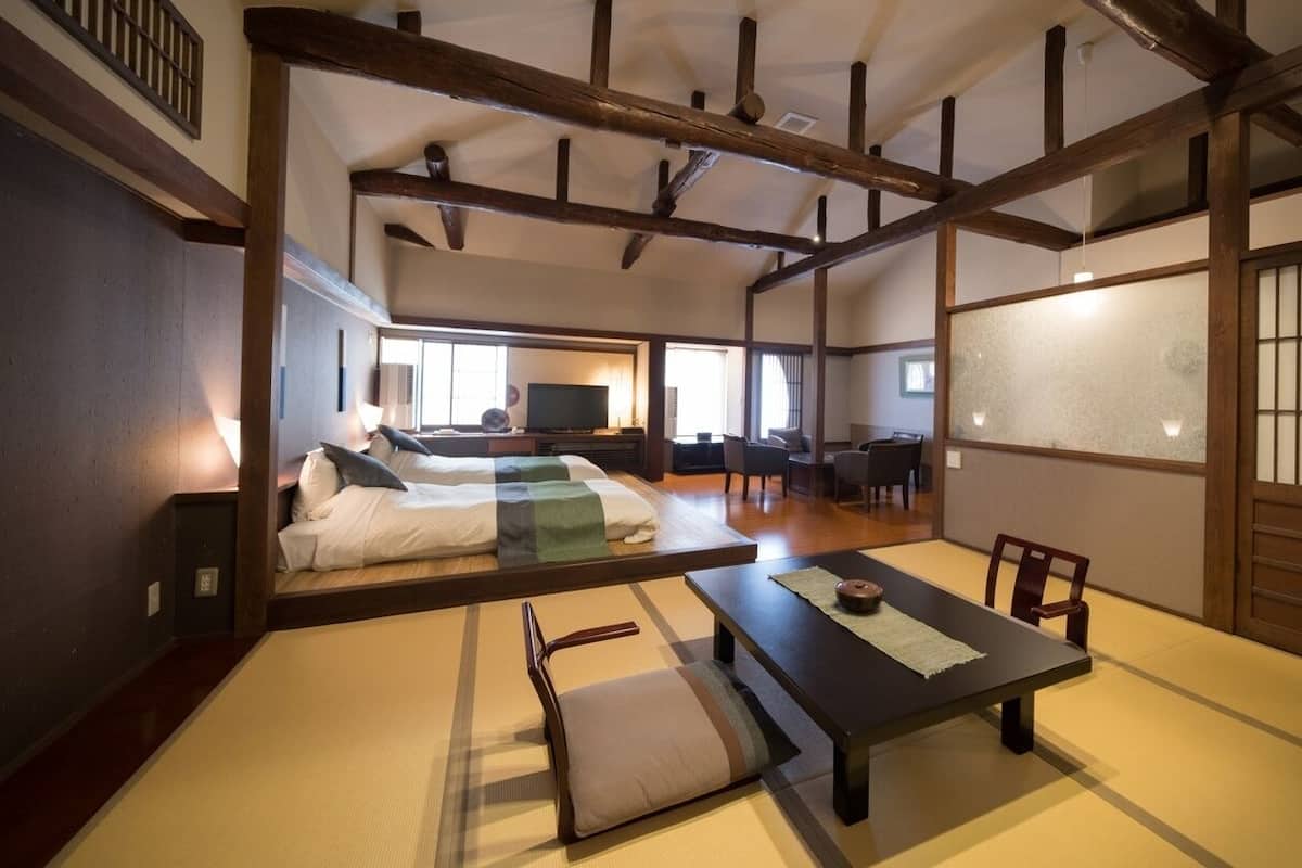 A traditional Japanese-style room with tatami flooring, a low table, and a bed with a futon.