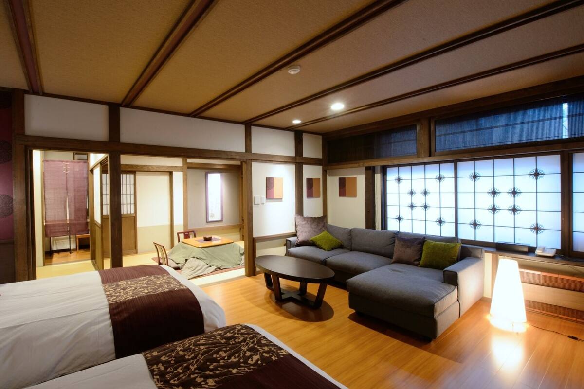 A traditional Japanese-style room with tatami flooring, a low table, a sofa, and a bed with a futon.