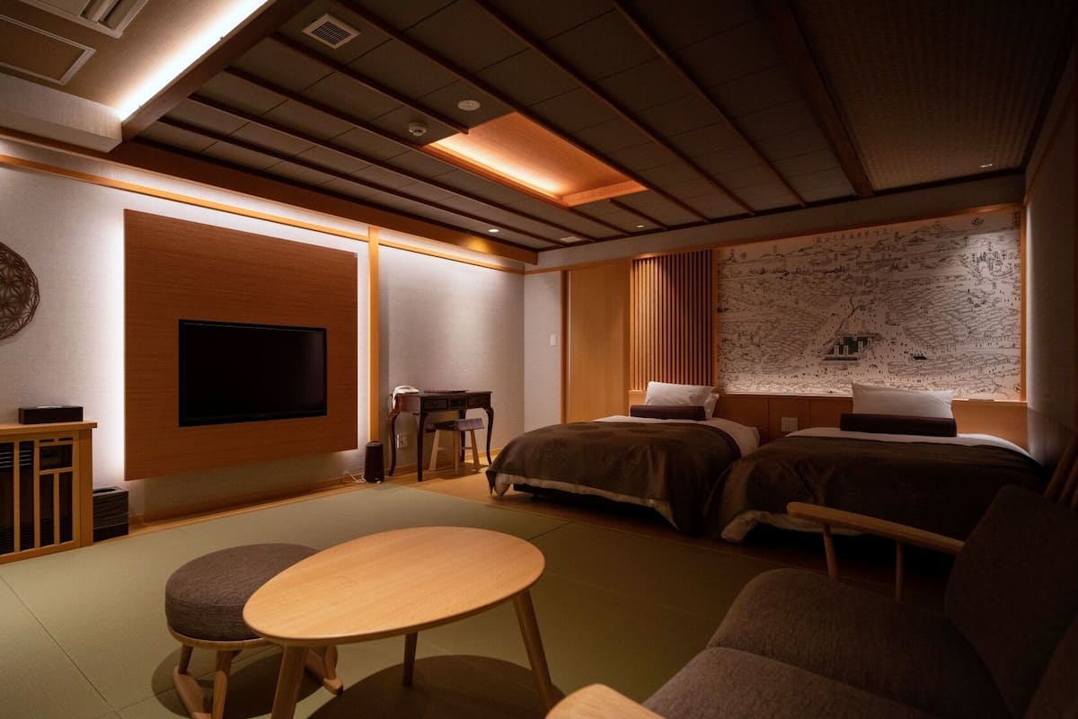A traditional Japanese-style room with tatami flooring, a low table, a sofa, a bed, and a wall-mounted TV.