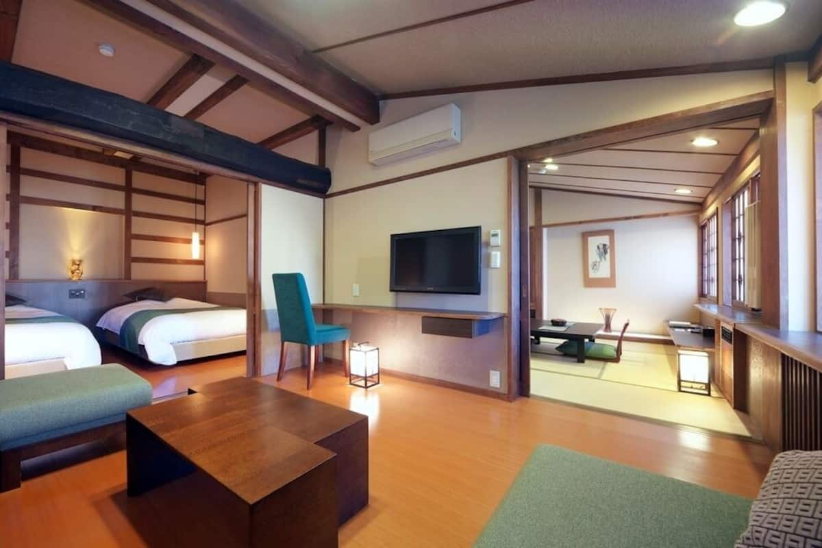 Habitación de hotel con techo de madera, dos camas, televisión, escritorio y zona de estar con cojines.