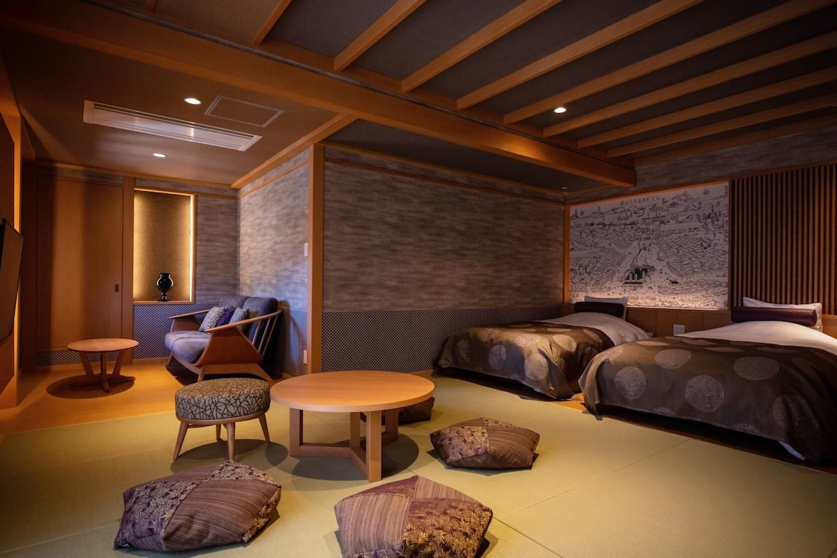 A modern hotel room with a wooden ceiling, two beds, a seating area with a table and chairs, and a wall with a detailed map.