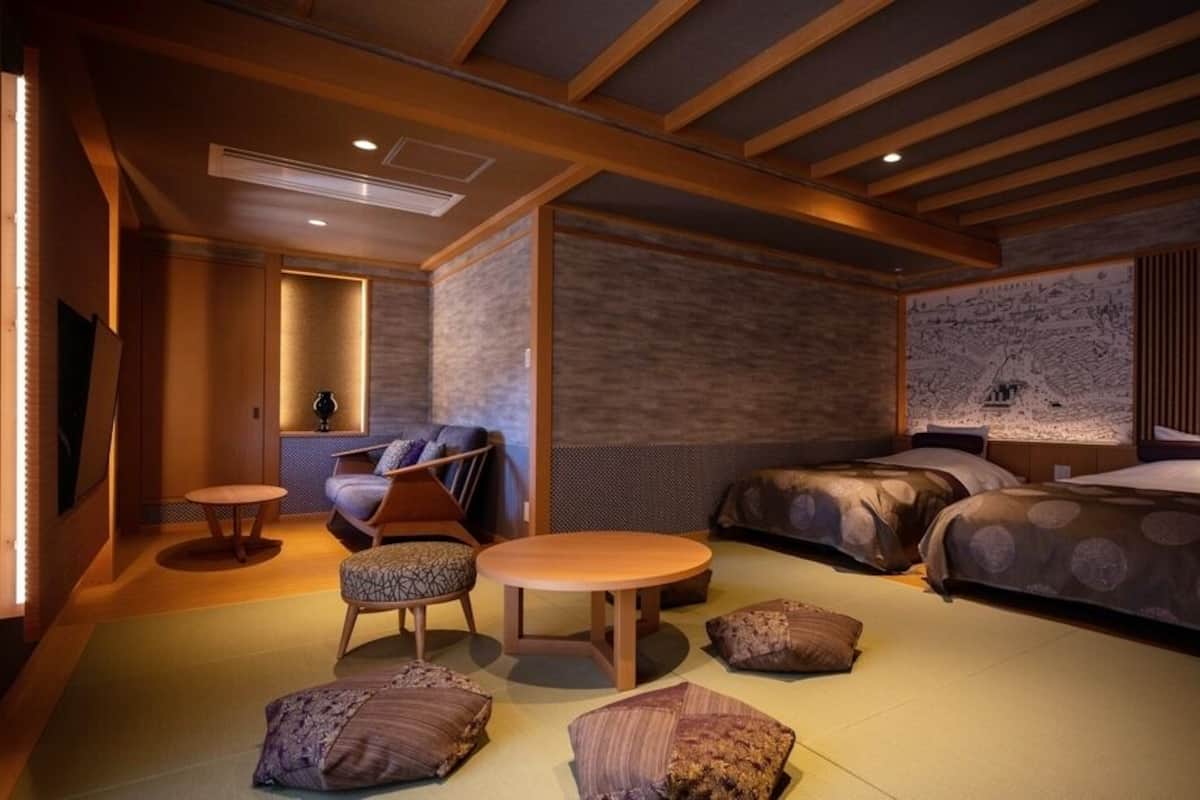 A room with two beds, a round table, a sofa, and a small table with a lamp.