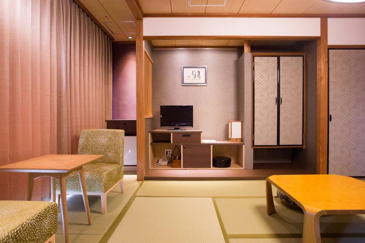 Una camera tradizionale in stile giapponese con pavimento in tatami, un tavolino, un divano, un televisore e un armadio.