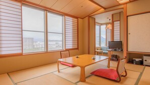 A traditional Japanese room with tatami flooring, a low table, a television, and a view of the city. - Notsu Ryokan (Matsue)