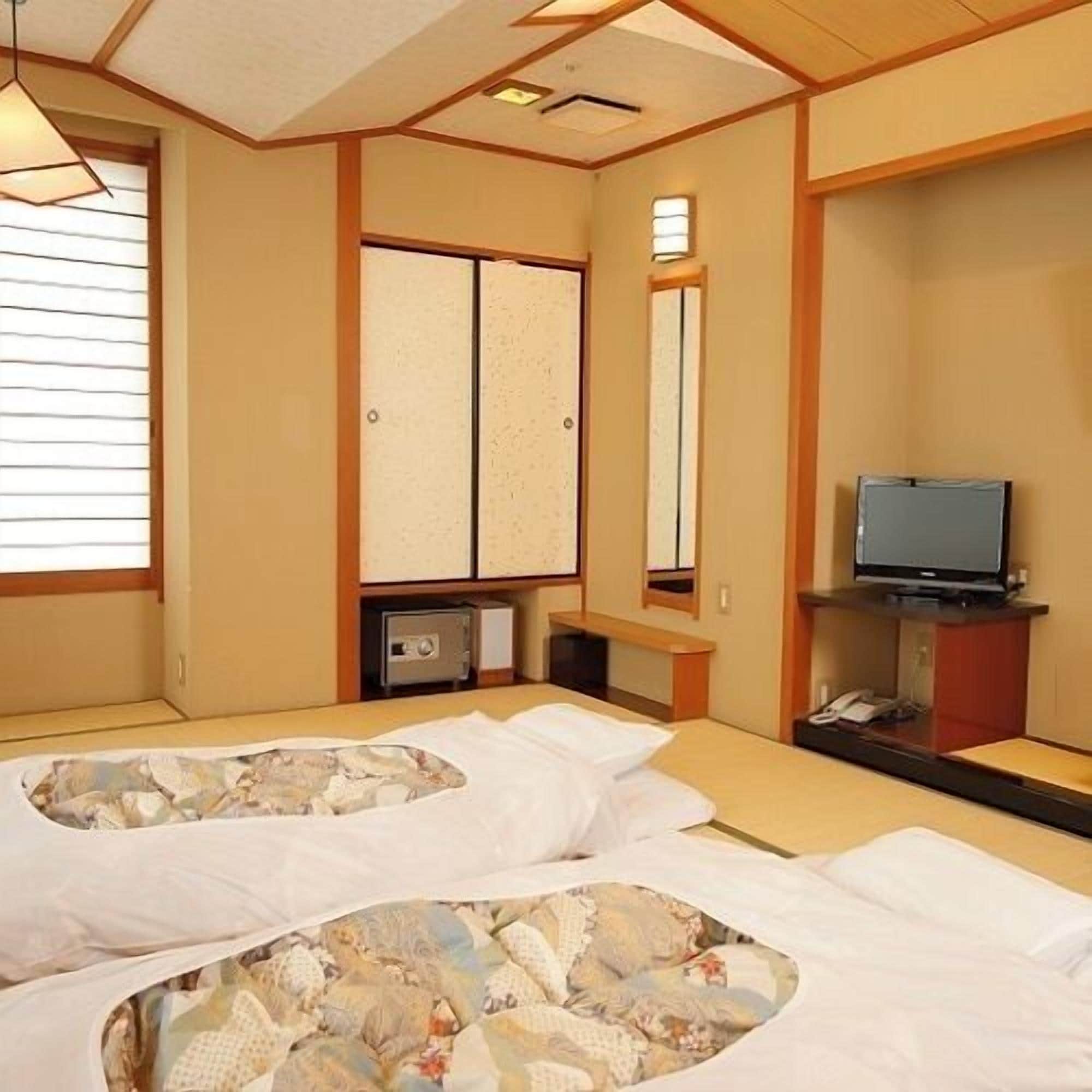 Une chambre d’hôtel avec deux lits, une télévision et une porte coulissante de style japonais traditionnel.