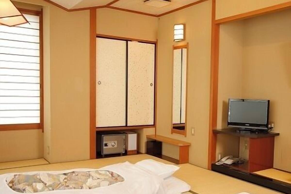 Una camera d'albergo con due letti, una televisione e una porta scorrevole tradizionale giapponese.