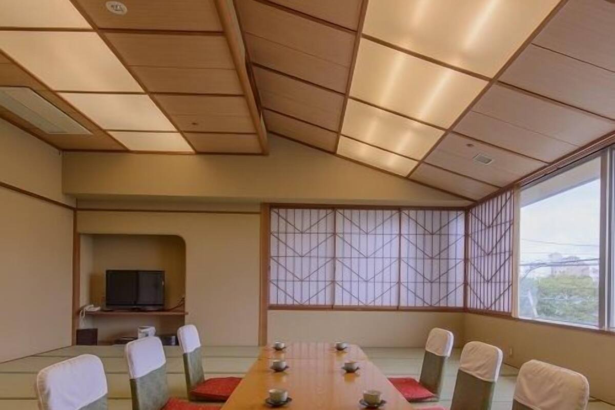 Una sala conferenze con un lungo tavolo, cuscini rossi e una televisione sullo sfondo.