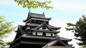 A traditional Japanese castle with multiple tiers and a stone base, surrounded by well-maintained greenery. - Notsu Ryokan (Matsue)