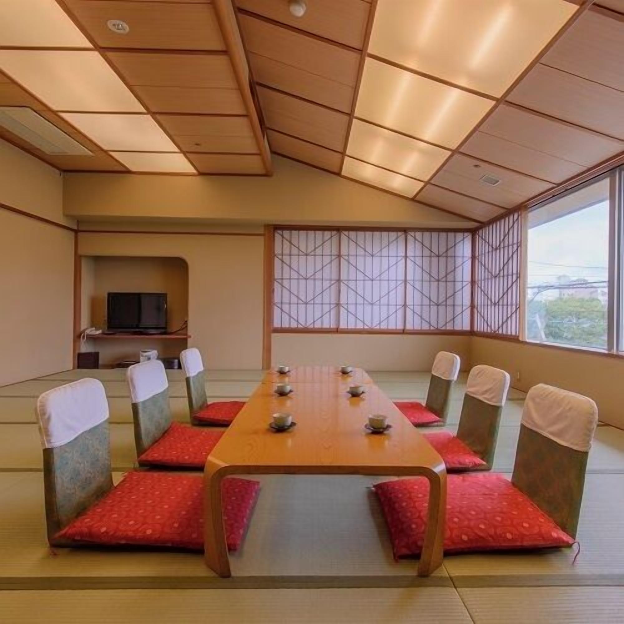 Une pièce de style japonais traditionnel, avec un sol recouvert de tatamis, une petite table basse entourée de coussins et un téléviseur placé dans un coin.