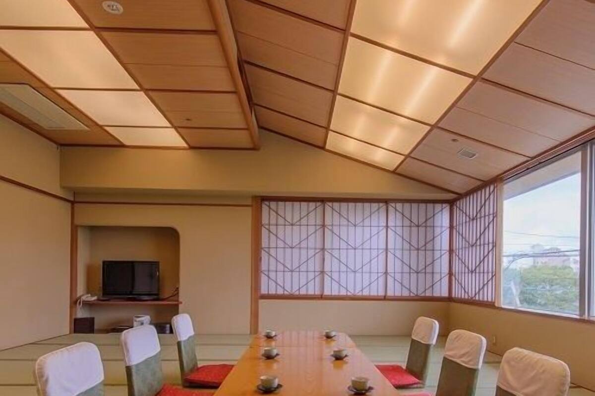 Una tradizionale stanza in stile giapponese con pavimento in tatami, un tavolino con cuscini e un televisore nell'angolo.