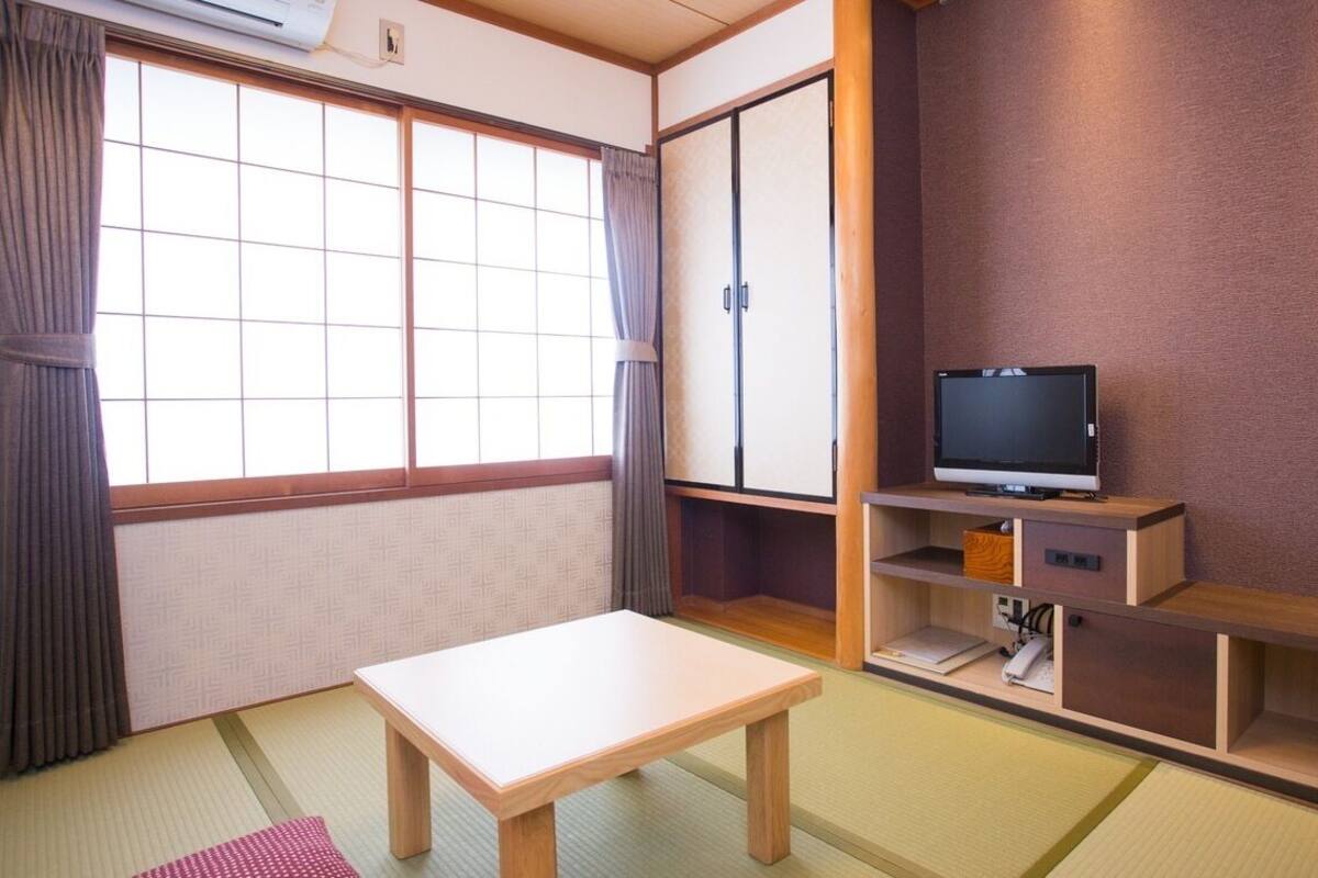 Una tradizionale stanza giapponese con pavimento in tatami, un tavolino in legno, un televisore su un supporto in legno e porte scorrevoli.