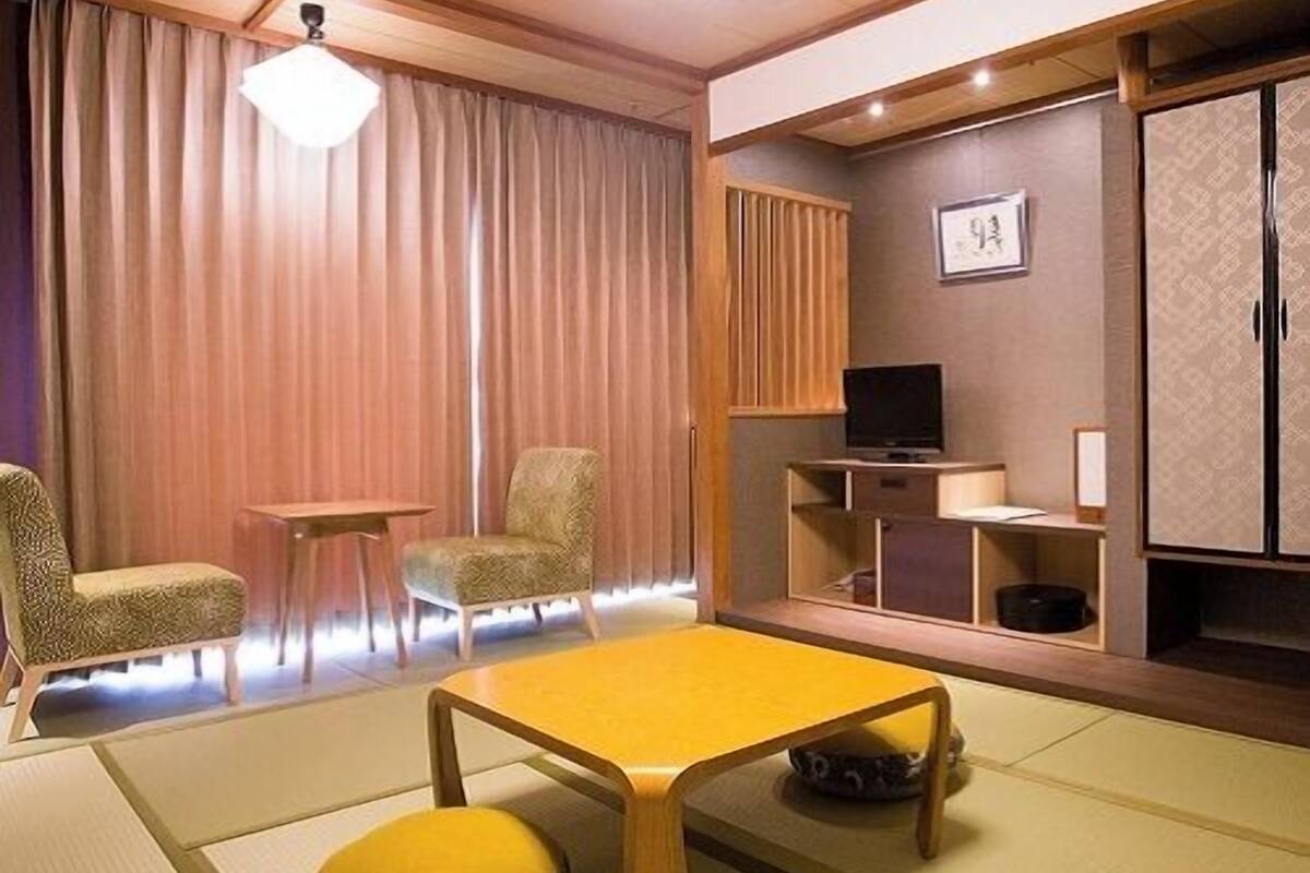 Una camera tradizionale giapponese con pavimento in tatami, un tavolino basso, un televisore e un armadio.