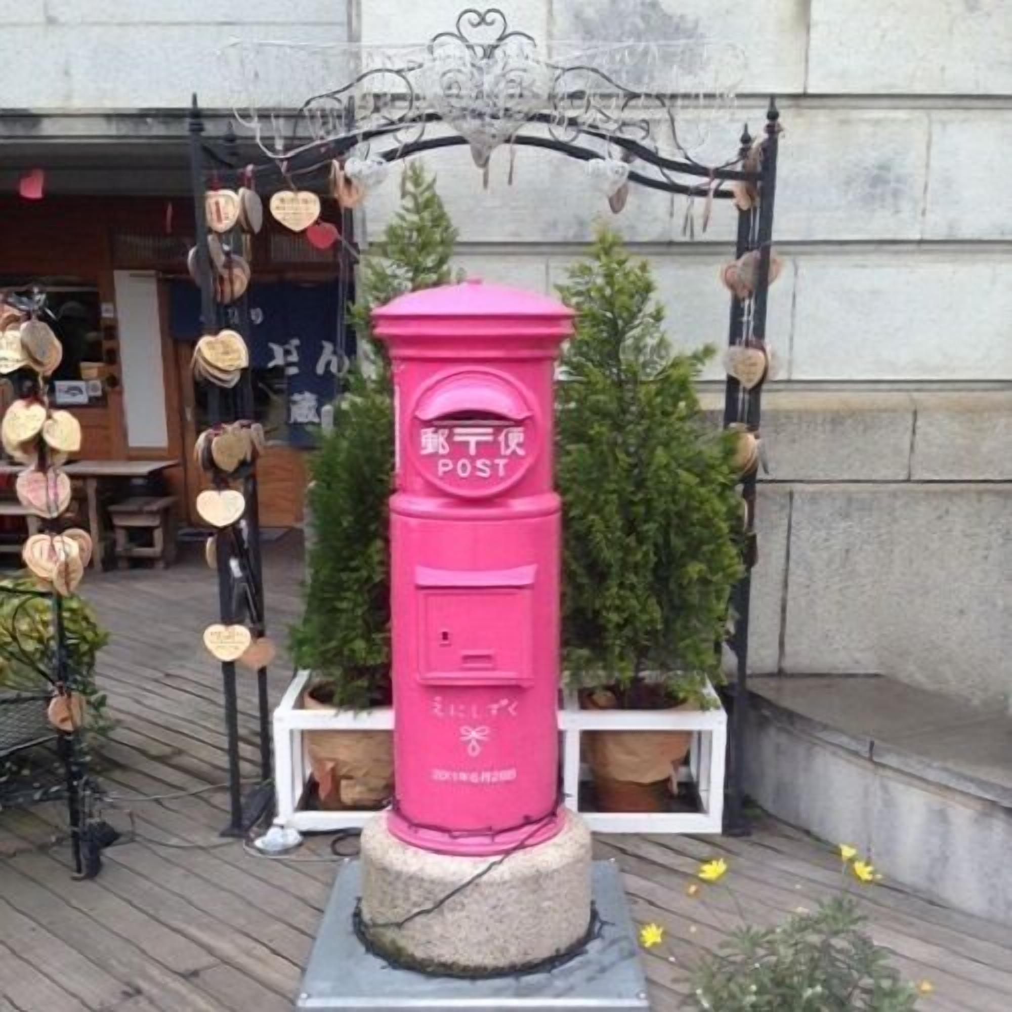 A pink mailbox with Japanese characters, surrounded by heart-shaped decorations and a small tree.