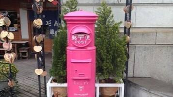 A pink mailbox with Japanese characters, surrounded by heart-shaped decorations and a small tree.