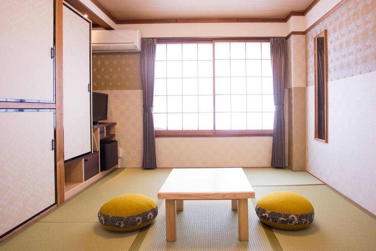 Una stanza tradizionale giapponese con pavimento in tatami, uno shoji scorrevole, un tavolo e due cuscini.