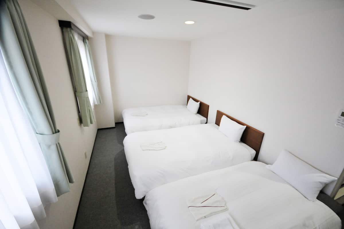 Habitación de hotel con tres camas individuales, una ventana con cortinas y suelo alfombrado.