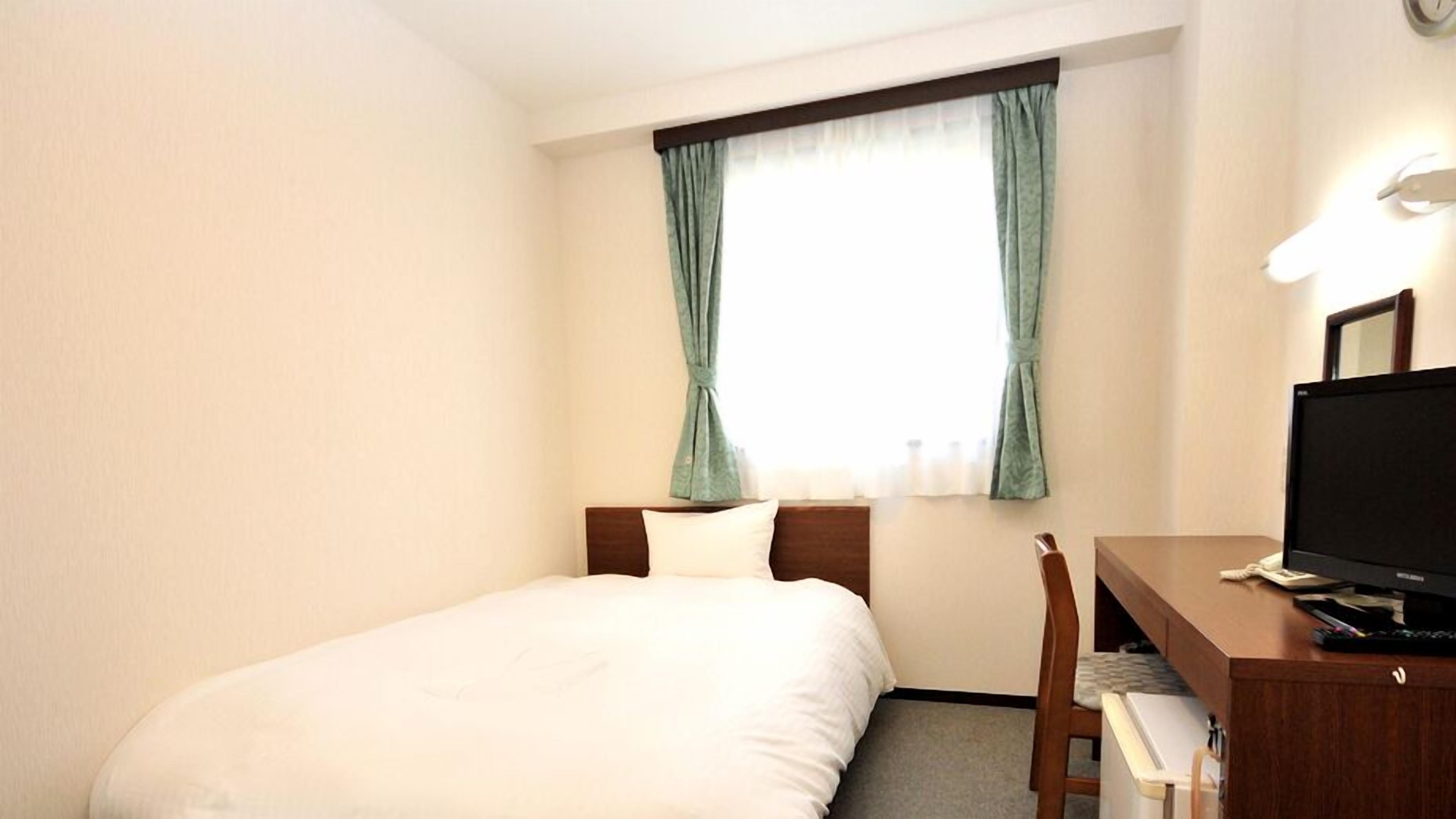Habitación de hotel con cama, escritorio con computadora, una silla y ventana con cortinas.