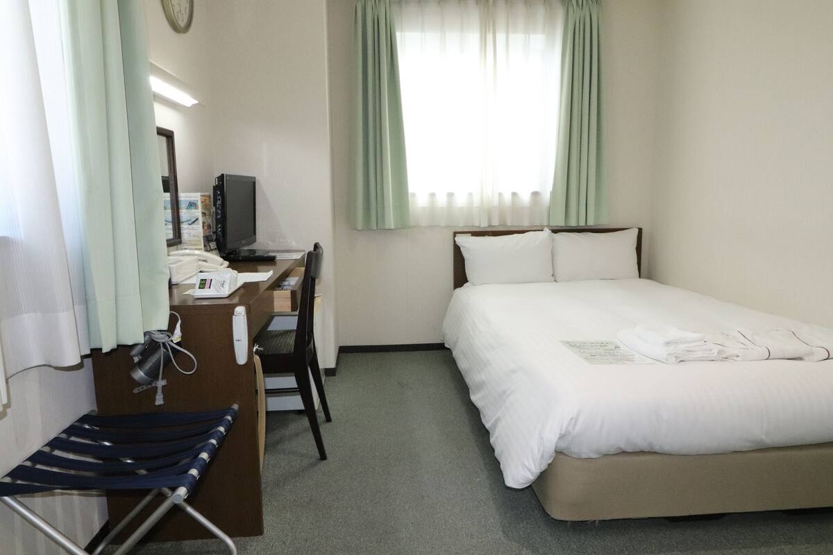 Habitación de hotel con cama, escritorio, computadora, silla y una mesita con teléfono.