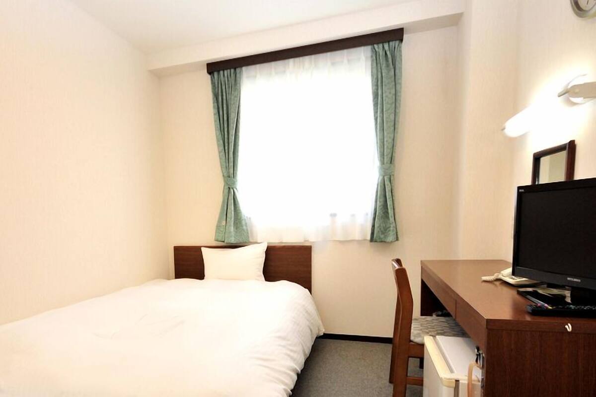 Habitación de hotel con cama, escritorio con computadora, una silla y ventana con cortinas.