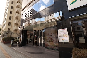 Entrada de hotel con fachada de vidrio, una escalera y un cartel anunciando tarifas de habitaciones.
