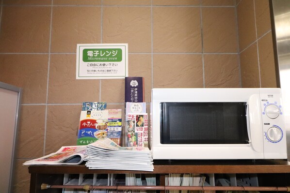 Un horno microondas sobre una repisa con un cartel arriba y varios objetos, como revistas y un libro.