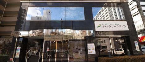 A hotel entrance with a glass facade, a staircase leading to the entrance, and a signboard with Japanese text.