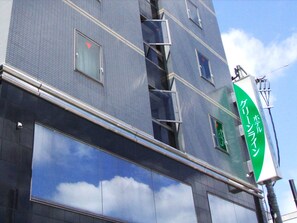 A multi-story building with large windows reflecting clouds, a green sign with Japanese characters, and a visible fire escape. - Hotel Green Line (Sendai)
