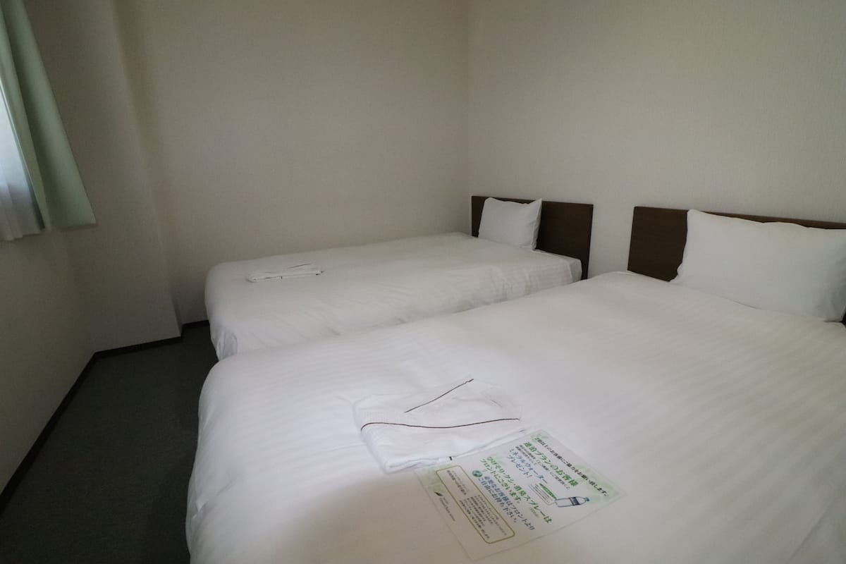 Dos camas individuales con sábanas blancas y cabeceros marrones en una habitación de hotel.