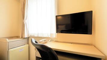 Habitación de hotel compacta con cama, escritorio, silla, televisión y refrigerador pequeño.