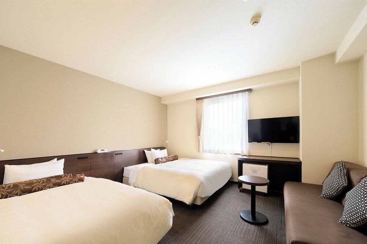 A hotel room with two beds, a sofa, a TV, and a desk.