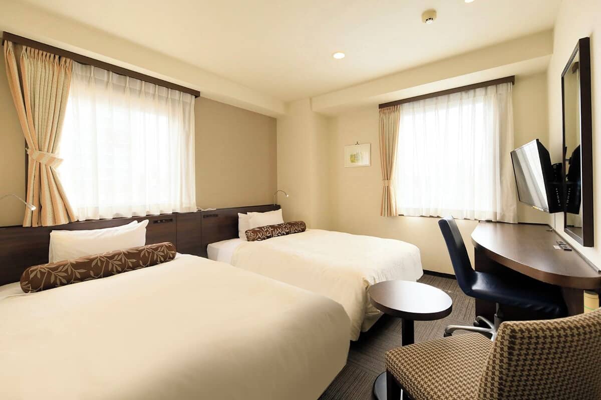 A hotel room with two beds, a desk, a chair, and a television.