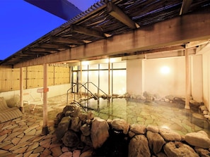 A stone-tiled outdoor hot spring area with a wooden pergola, a white chair, and a small waterfall feature. - Aomori Center Hotel (Aomori)