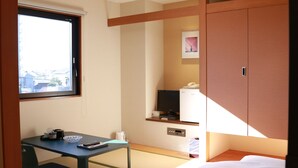 Una habitación con cama, escritorio, silla, televisor y ventana.