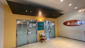 Un área de recepción con puertas de vidrio, una pequeña mesa con un cartel y un cartel en la pared con texto en japonés.