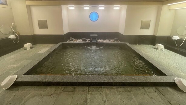 Un área de spa con un elemento central de agua, bancos y un accesorio de luz circular en el techo.