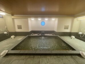 Un área de spa con un elemento central de agua, bancos y un accesorio de luz circular en el techo.