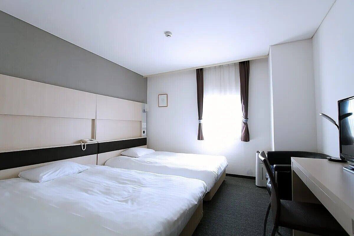 A hotel room with two beds, a desk, a chair, a television, and a window with curtains.