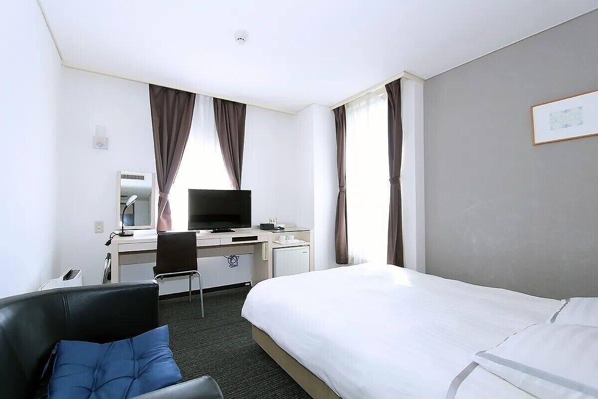 A hotel room with a bed, a desk with a computer, a chair, and a television.