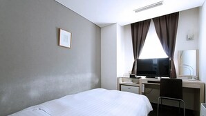 Habitación de hotel con cama, escritorio, computadora, silla y ventana con cortinas.