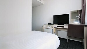 Habitación de hotel con cama, escritorio con televisor, silla y refrigerador pequeño.