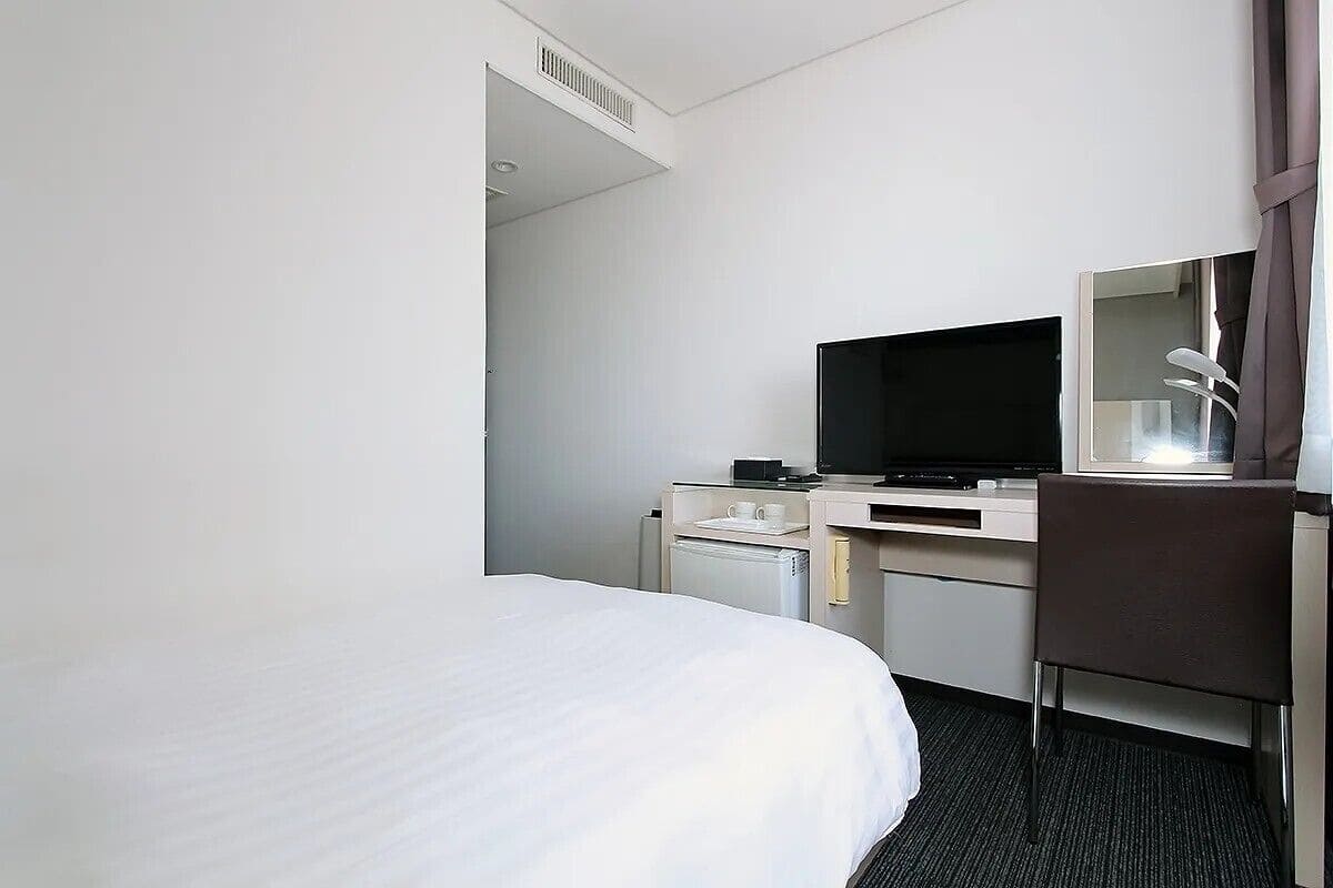 Habitación de hotel con cama, escritorio con televisor, silla y refrigerador pequeño.